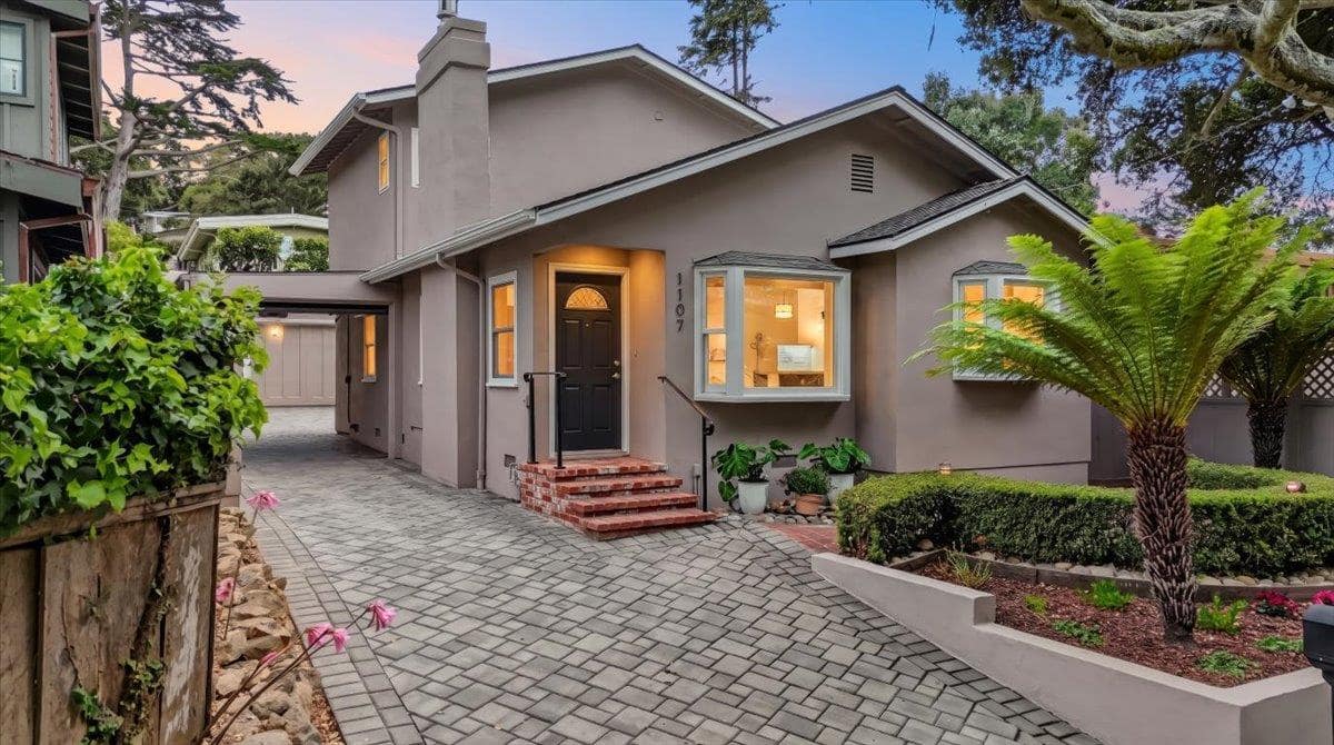 The house at dusk from its paved driveway, bay window and porch lights glowing, the number 1107 beside the door.