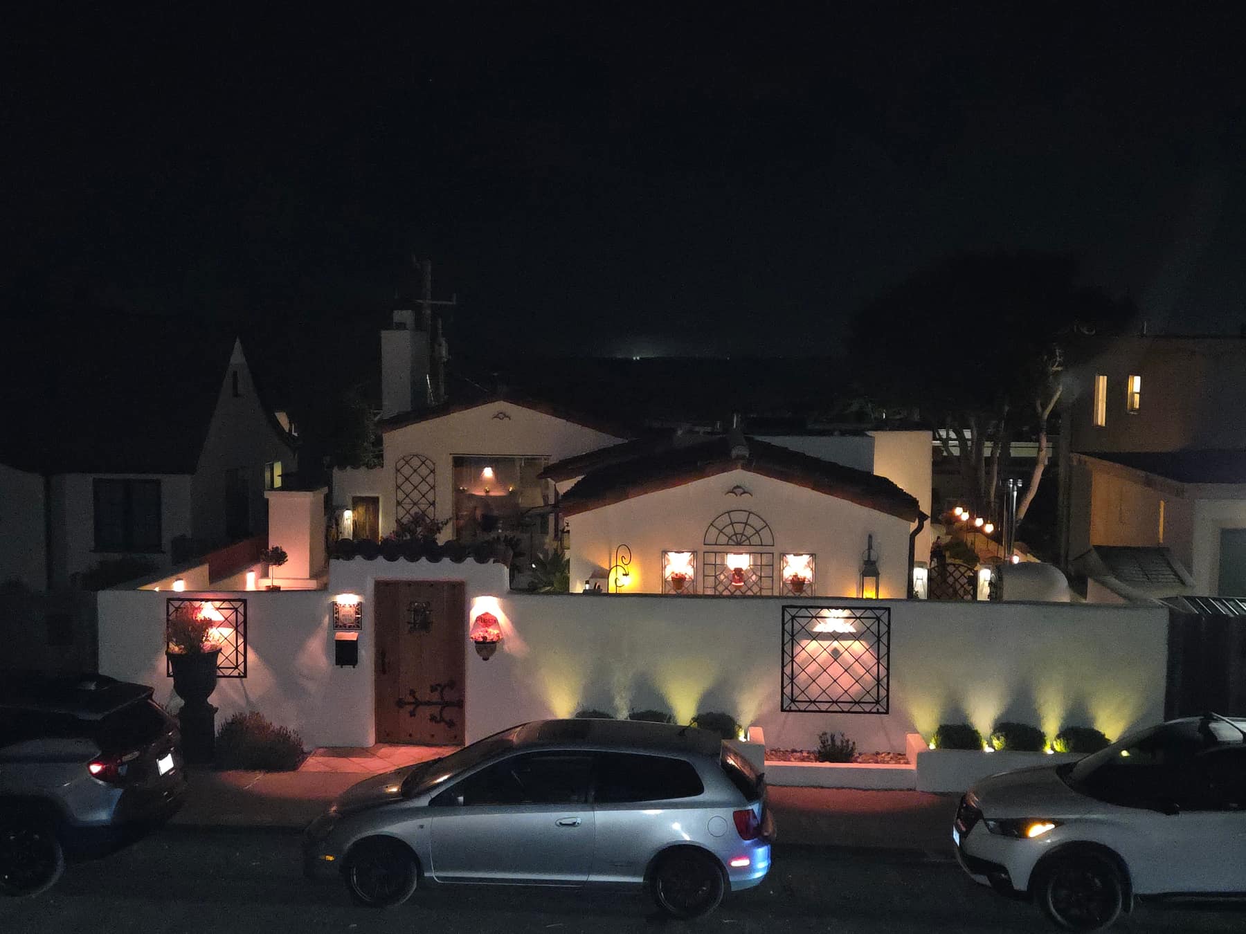 The house seen from across Lighthouse Avenue after dark, its white walls and tiled roofline lit from below.