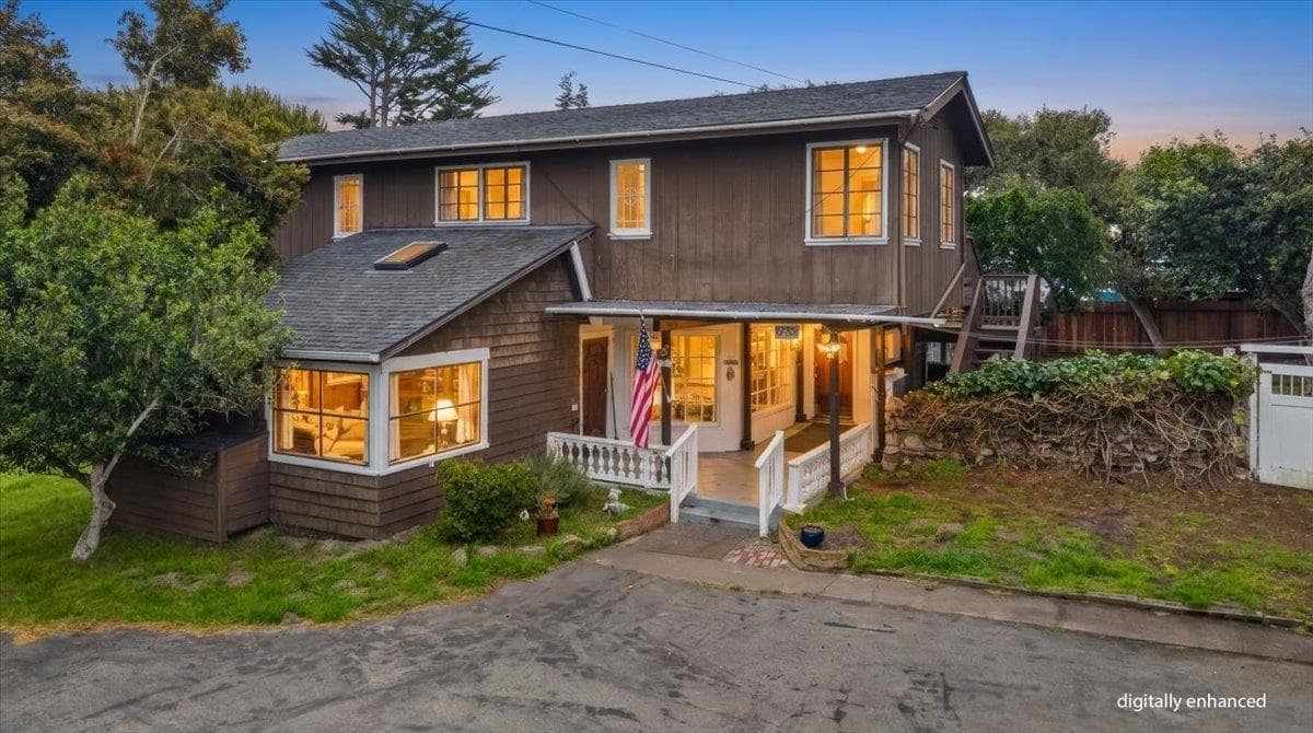 The two-storey shingled house at dusk, its windows lit and a flag on the porch.